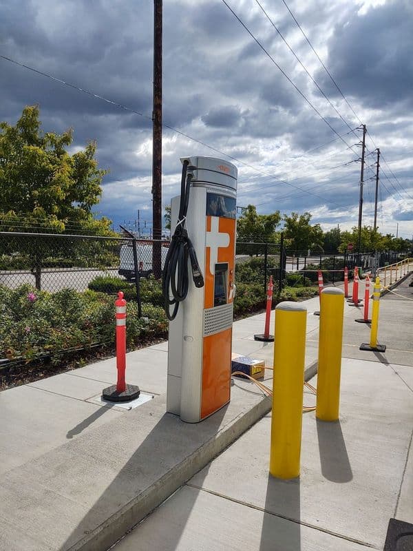 Electric vehicle charging station with orange and white design, surrounded by yellow and red safety barriers.