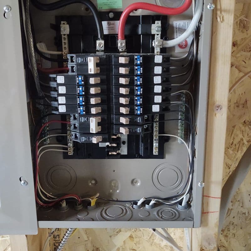 Electrical panel with circuit breakers and wiring in a wooden structure, showing organized connections.