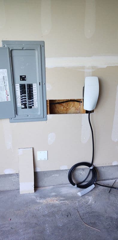 Electric vehicle charging station mounted on garage wall near electrical panel.