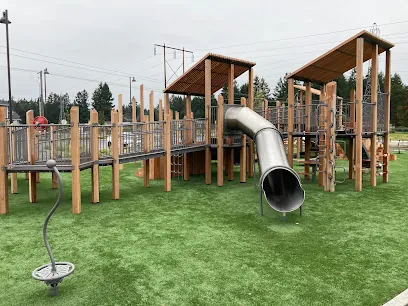 Wooden play structure with a metal tube slide and elevated walkways at Cross Park on artificial turf