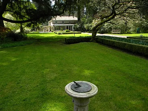 Sundial on a mowed lawn with a hedge and a house in the background at Lakewold Gardens