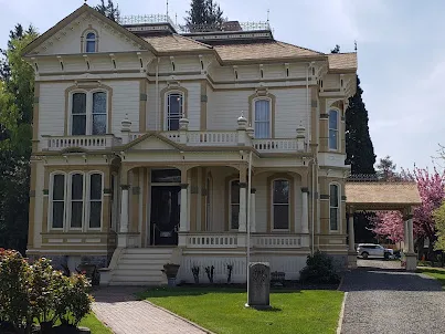 Yellow two-story Victorian Meeker Mansion with white trim, a front lawn and a flowering tree beside it