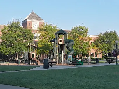 Playground with a slide and a brick clock tower behind trees at Pioneer Park in Puyallup