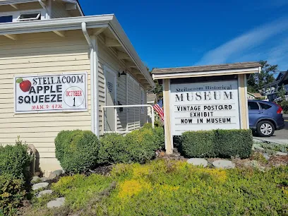 Steilacoom Historical Museum sign with a vintage postcard exhibit notice beside a yellow building